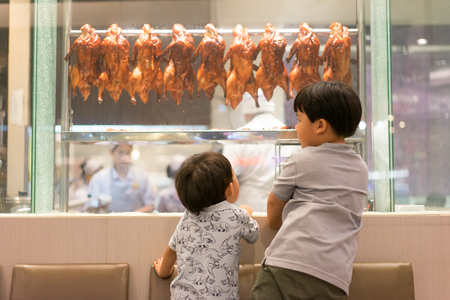 2 hungry brothers are watching a chef preparing roasted duck in Chinese restaurantの写真素材
