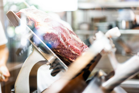 A chef is slicing a raw beef by meat slicer for shabu shabu in the japanese restaurant.の写真素材
