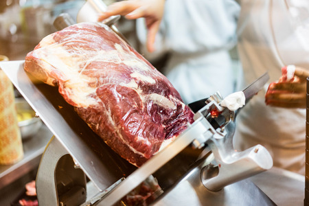 A chef is slicing a raw beef by meat slicer for shabu shabu in the japanese restaurant.