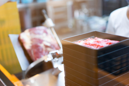 A chef is slicing a raw beef by meat slicer for shabu shabu in the japanese restaurant.