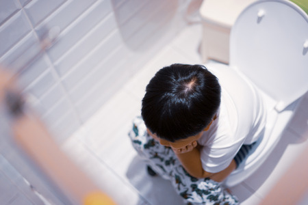 A boy is sitting on toilet with suffering from constipation or hemorrhoid.の写真素材