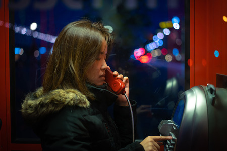 A woman is talking on a public telephone at night on the street.