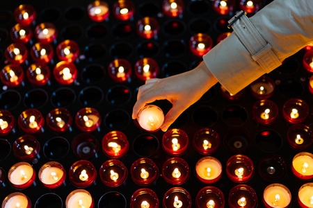 A woman is holding candle and praying near altar in church.