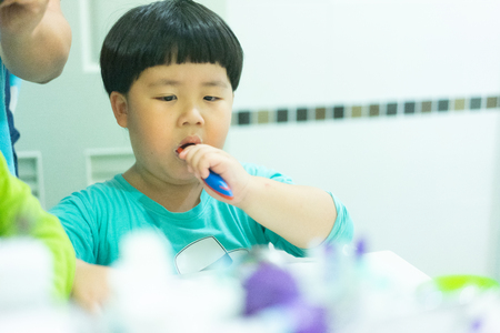 A boy try to brushes his teeth by himself in the restroom at night, before he go to bed.の写真素材