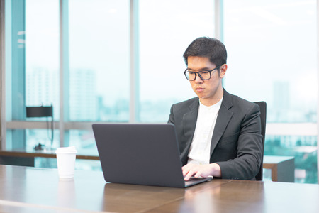 a businessman is working seriously with his laptop computer and he have a cup of hot coffee on the table.の写真素材