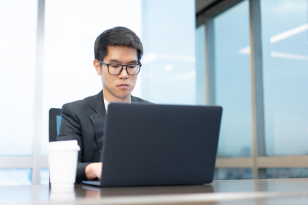 a businessman is working seriously with his laptop computer and he have a cup of hot coffee on the table.の写真素材