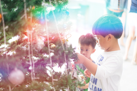 brothers are  decorating a Christmas tree with present and mirror balls.の写真素材