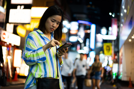 A woman is shopping online at the night street in the city.の写真素材