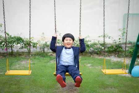 A boy is playing a swing with his brother at the outdoor playground.