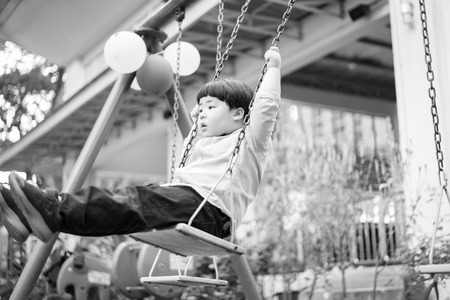 A boy is playing a swing with his brother at the outdoor playground.の写真素材
