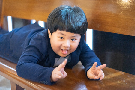 A naughty boy makes funny face, he is playing In the church with formal suit.の写真素材