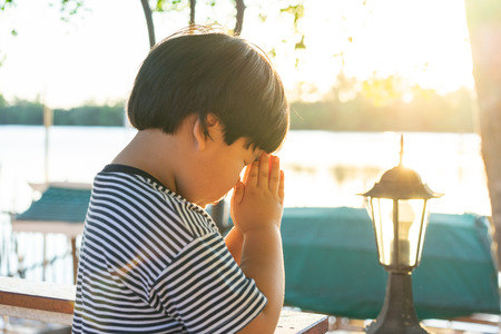 A little prayer, A boy is praying seriously and hopefully to Jesus beside the river with the sunset moment during the evening.の写真素材