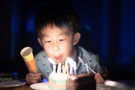 A happy kid is blowing candles on his birthday cake in the dark at his birthday party night.