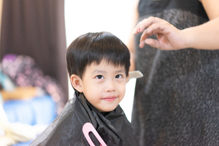 Grandmother is cutting hair of her cute grandson at home.の写真素材