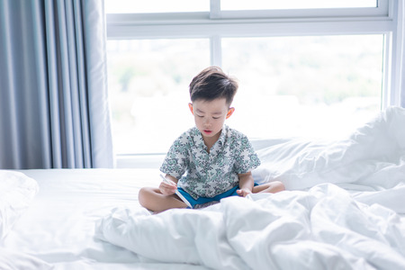 A boy is drawing on the tablet on the bad.の写真素材