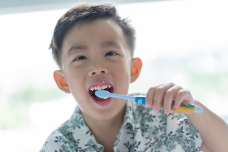 A cute boy is brushing his teeth in the morning on the bed.