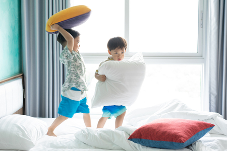 2 cute brothers are jumping and playing in the morning on the bed.の写真素材
