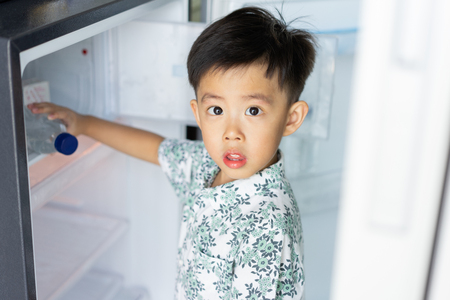 The boy is helping his mother to work at home and picking up water from fridge to his mom.の写真素材