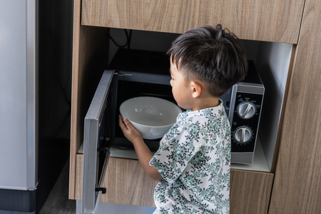 A boy is cooking his breakfast by microwave in kitchen in the morningの写真素材