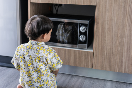 A boy is cooking his breakfast by microwave in kitchen in the morningの写真素材