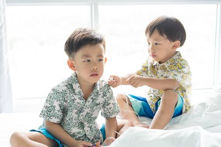 2 cute brothers are listening the song with cell phone in the morning on the bed.の写真素材