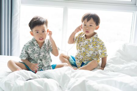 2 cute brothers are listening the song with cell phone in the morning on the bed.の写真素材