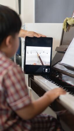 A boy is learning piano online with a tablet by the social network in his house.の写真素材