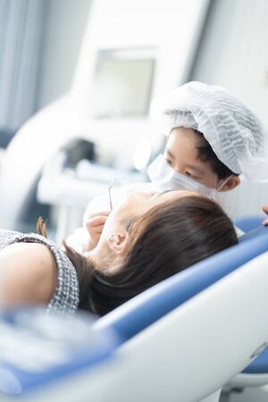 Little Asian dentist boy with a dentist suit try to check his patient teeth in the dentist clinic: Future career and career dream concept.の写真素材