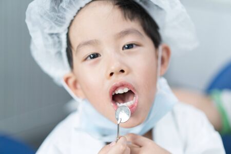 Little Asian dentist boy with a dentist suit try to check his patient teeth in the dentist clinic: Future career and career dream concept.の写真素材