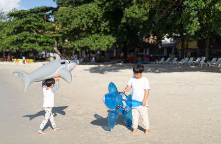 Brothers are playing the sea and sand. Little baby boys with inflatable toy float playing in the water on summer vacation in a tropical resort. Kids with toy shark and dolphin on a beach holiday.の写真素材