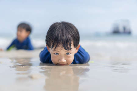 brothers are playing in the sand and swimming at the beach at an island in Thailandの写真素材