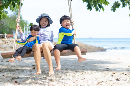 Mother playing on the swing with her children at the beach on holiday.の写真素材