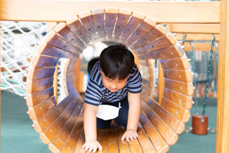 A boy is in a wooden tunnel at a playground.の写真素材