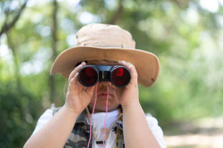 An adventure boy is using a binocular while he travels the jungle.の写真素材