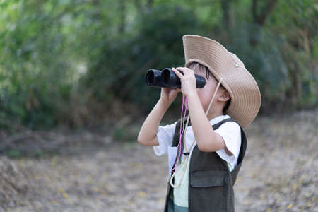 An adventure boy is using a binocular while he travels the jungle.の写真素材