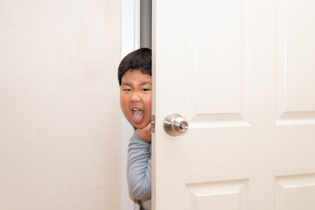 A playful boy peeking from behind the door of the house.の写真素材