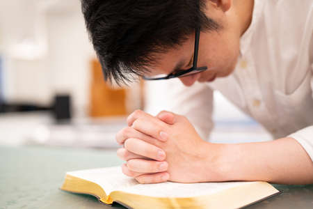Asian man is reading the Holy Bible and praying in a worship room in a Christian church.