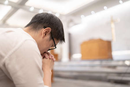 An Asian man praying on a bench in a Christian church.の写真素材