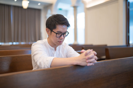 An Asian man praying on a bench in a Christian church.の写真素材