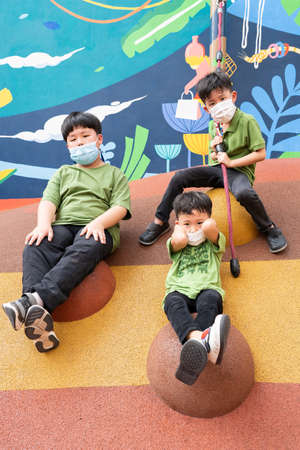 3 brothers are playing with face masks on playground during quarantineの写真素材
