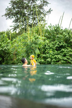 On a hot summer day, a father and son have fun in the water pool. Swimming and leisure activities are popular during vacations.の写真素材