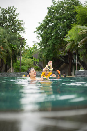 On a hot summer day, a father and son have fun in the water pool. Swimming and leisure activities...