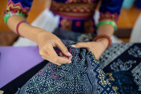 A tribal native fabric is sewn on the hand of an Asian woman (dyed indigo color). Folk art and...