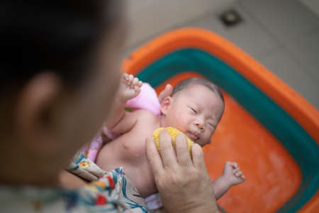 Mother is bathing her child in an orange tub.の写真素材