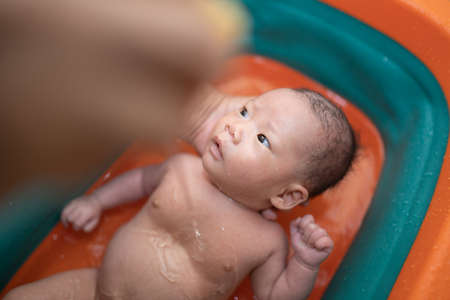 Mother is bathing her child in an orange tub.