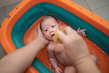 Mother is bathing her child in an orange tub.の写真素材