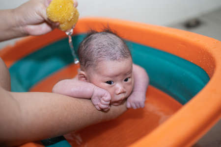 Mother is bathing her child in an orange tub.の写真素材