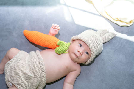 A baby girl dresses up a bunny, playing her carrot pillow.の写真素材