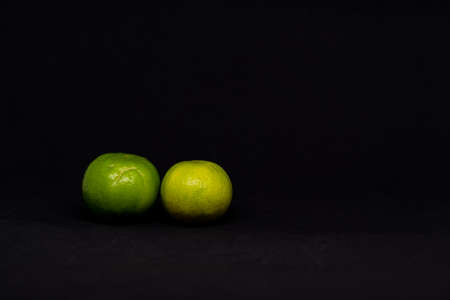 Two lemons have both green and yellow with black background.の写真素材