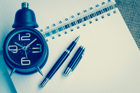 Vintage alarm clock ,notebook and pen on sackcloth backgroundの写真素材